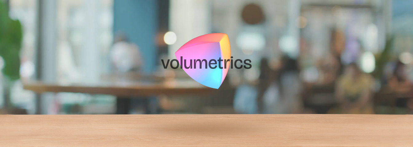 The Volumetrics logo floating above a wooden table, with a coffee shop scene blurred in the background